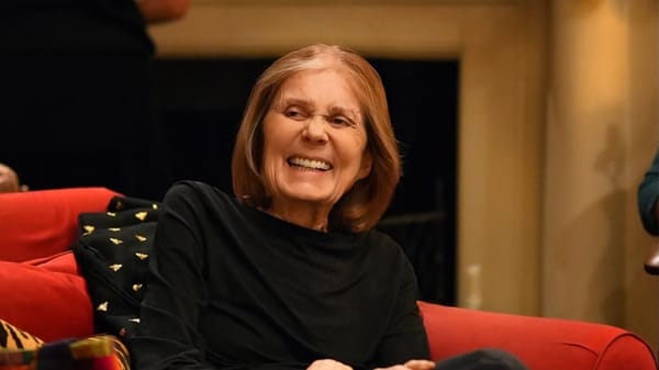 Gloria Steinem smiling while seated in a red chair.